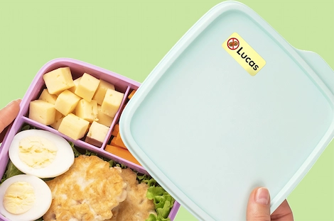 Open lunchbox met eten erin, met op het deksel een geel naamlabel met een notenallergiesymbool